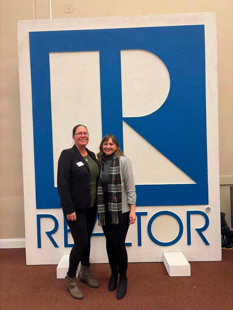 two women in front of realtor sign
